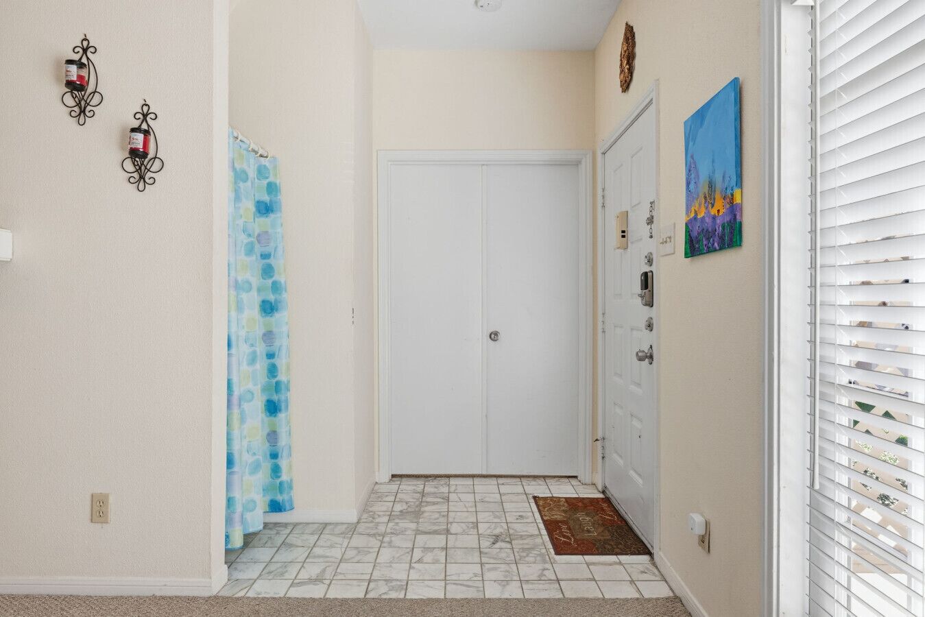 A hallway with a tiled floor, a white door, a blue shower curtain, and a painting on the wall.