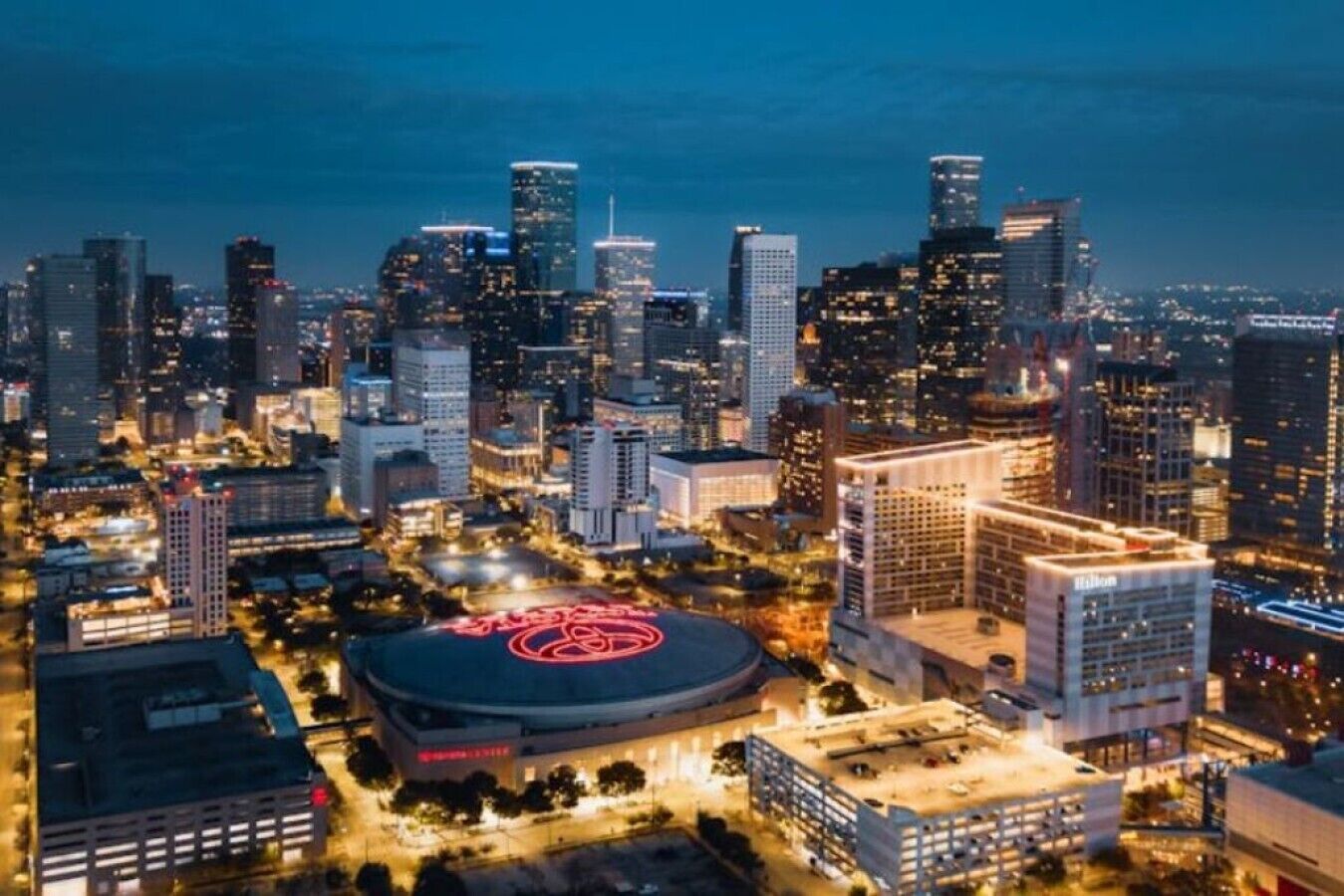 A cityscape at night with illuminated buildings and a large circular structure in the foreground.