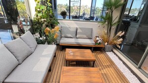 Un espace extérieur moderne, aménagé avec une terrasse en bois, un canapé gris et deux tables en bois.