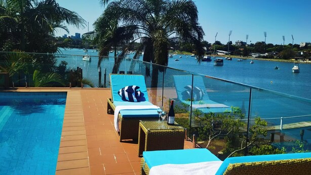 Un espace piscine doté de chaises longues et d’une rambarde en verre donnant sur un port de plaisance où sont amarrés des bateaux.