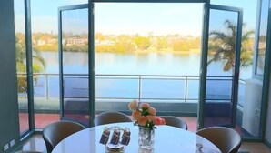 Une table ronde entourée de six chaises, un vase rempli de fleurs et une vue sur un lac, visible à travers de grandes portes vitrées.