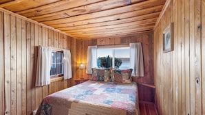 Une chambre dans une cabane en bois, avec un grand lit, une fenêtre avec des rideaux et une vue sur l’extérieur.