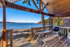 Une terrasse en bois avec un barbecue et des tables, donnant sur un lac.
