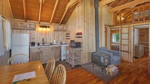 A wooden cabin interior with a kitchen, dining area, and a fireplace. - 2BR Beachfront Cabin w/ loft - steps from prime west-facing beach! (Eastsound)