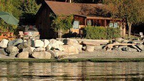 A rustic cabin with a wooden exterior, a porch, and a car parked nearby. - 2BR Beachfront Cabin w/ loft - steps from prime west-facing beach! (Eastsound)