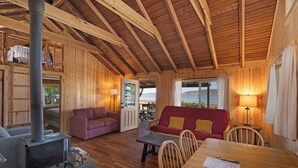 A cozy cabin interior with a wood stove, wooden furniture, and a view of the outdoors. - 2BR Beachfront Cabin w/ loft - steps from prime west-facing beach! (Eastsound)