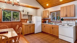 A kitchen with wooden cabinets, a white refrigerator, a microwave, a stove, and a dining table with chairs. - 2BR Ocean View Cabin - 1 min walk to world class beach! (Eastsound)