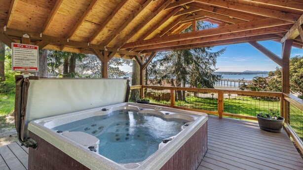 Una terraza de madera con un jacuzzi, un letrero con las normas del spa y vista al océano.