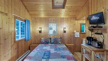 A wooden cabin room with a bed, a television, and a small kitchenette.