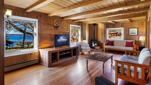 A wooden interior with a TV, fireplace, and seating area. - 3BR Ocean View Farmhouse - 1 min walk to prime west-facing beach! (Eastsound)