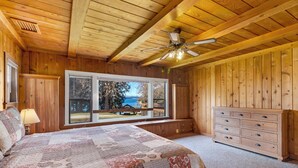 A wooden cabin bedroom with a large bed, a dresser, and a view of a lake. - 3BR Ocean View Farmhouse - 1 min walk to prime west-facing beach! (Eastsound)