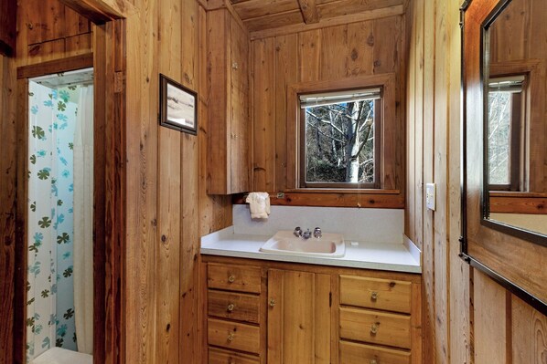 Une salle de bain rustique, avec des murs en bois, une fenêtre, un lavabo et des meubles en bois.