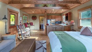 A cozy cabin interior with a wooden ceiling, a large bed, a dining area, and a kitchen. - Partial View Cabin w/ Hot Tub - 2 min walk to west-facing beach! (Eastsound)