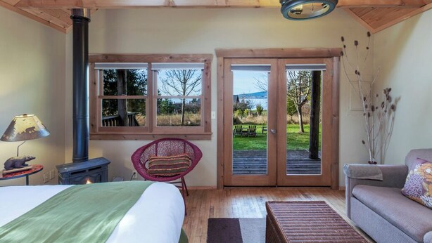 A bedroom with a bed, a chair, a sofa, a fireplace, and a view of the outdoors. - Partial View Cabin w/ Hot Tub - 2 min walk to west-facing beach! (Eastsound)