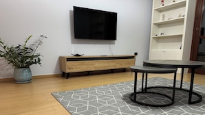 A modern living room with a flat-screen TV mounted on the wall, a wooden cabinet, a round table, and a patterned rug. - Charming 2-bedroom apartment with WiFi, AC in fabulous Tiranë (Tiranë)