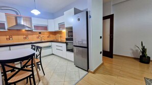 A modern kitchen with white cabinets, a stainless steel refrigerator, and a dining area with a table and chairs. - Charming 2-bedroom apartment with WiFi, AC in fabulous Tiranë (Tiranë)