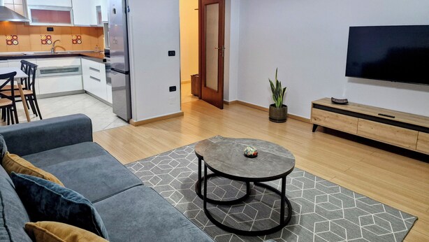 A modern living room with a grey sofa, a coffee table, and a TV on a wooden stand. - Charming 2-bedroom apartment with WiFi, AC in fabulous Tiranë (Tiranë)