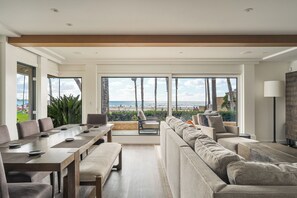 Un vaste espace de vie avec une grande fenêtre donnant sur une plage, une table à manger avec des chaises et un canapé.