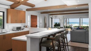 A modern kitchen with a large island, wooden beams, and a view of the beach.