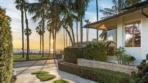 A modern house with a paved driveway, palm trees, and a view of the ocean.