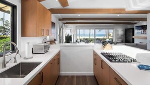 A modern kitchen with wooden cabinets, a central island, and a view of the beach.