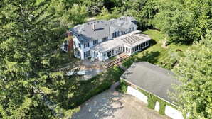 A large, two-story house with a spacious deck and multiple windows, surrounded by dense greenery. - Newly renovated, 7700 Sq. Ft,  8BR, 7BTH, Heated Pool, Hot Tub, Arcade Game Barn (Sawyer)