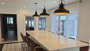 A modern kitchen with a long island, bar stools, pendant lights, and a view of the outdoor patio. - Newly renovated, 7700 Sq. Ft,  8BR, 7BTH, Heated Pool, Hot Tub, Arcade Game Barn (Sawyer)
