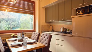 Uma cozinha moderna com área de jantar, apresentando uma mesa de madeira posta para dois, vista pela janela e eletrodomésticos embutidos.