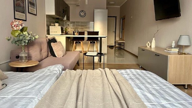 Une chambre d’hôtel moderne avec un grand lit, un canapé, une petite table ornée d’un vase de fleurs, un bureau avec une lampe et un téléviseur fixé au mur.