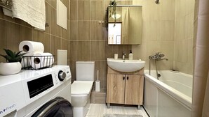 Une petite salle de bain équipée d’un lave-linge, de toilettes, d’un lavabo et d’une baignoire.