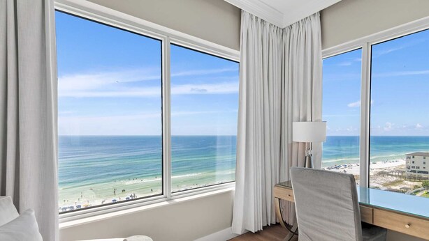 Ein Hotelzimmer mit großen Fenstern und Blick auf den Strand und den Ozean.