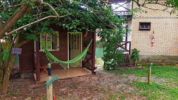 A wooden cabin with a hammock, a small porch, and a brick wall with a fire extinguisher. - Pousada Sol & Sal (Imbituba)
