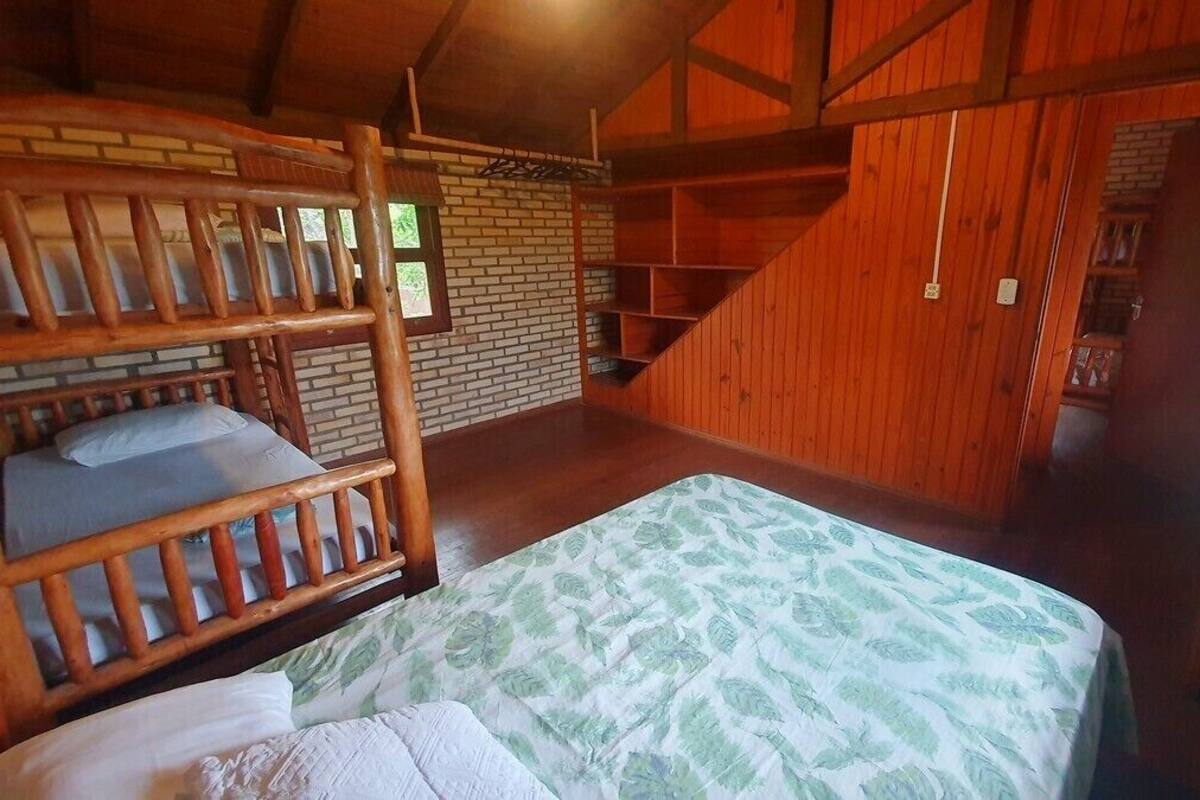 Un lit superposé en bois, recouvert d’une courtepointe à motifs de feuilles vertes, avec un mur en briques et un escalier en bois.