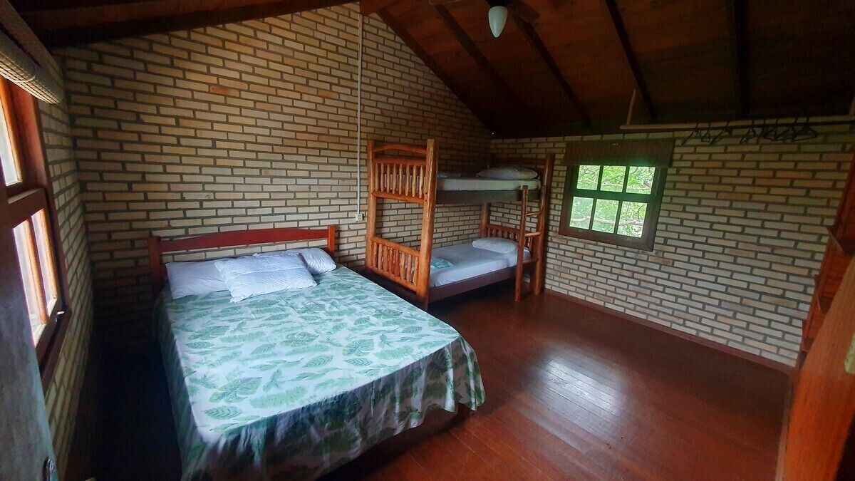 A room with a bunk bed, a single bed, wooden flooring, brick walls, and a window.