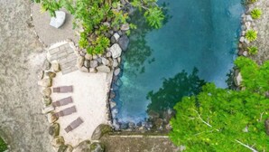 Une piscine d’un bleu éclatant, entourée de rochers et de verdure, avec un sentier de pierre menant à un espace aménagé pour s’asseoir.