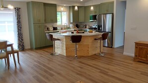 Een moderne keuken met groene kastjes, een centraal eiland met krukken, roestvrijstalen apparatuur en een houten vloer.