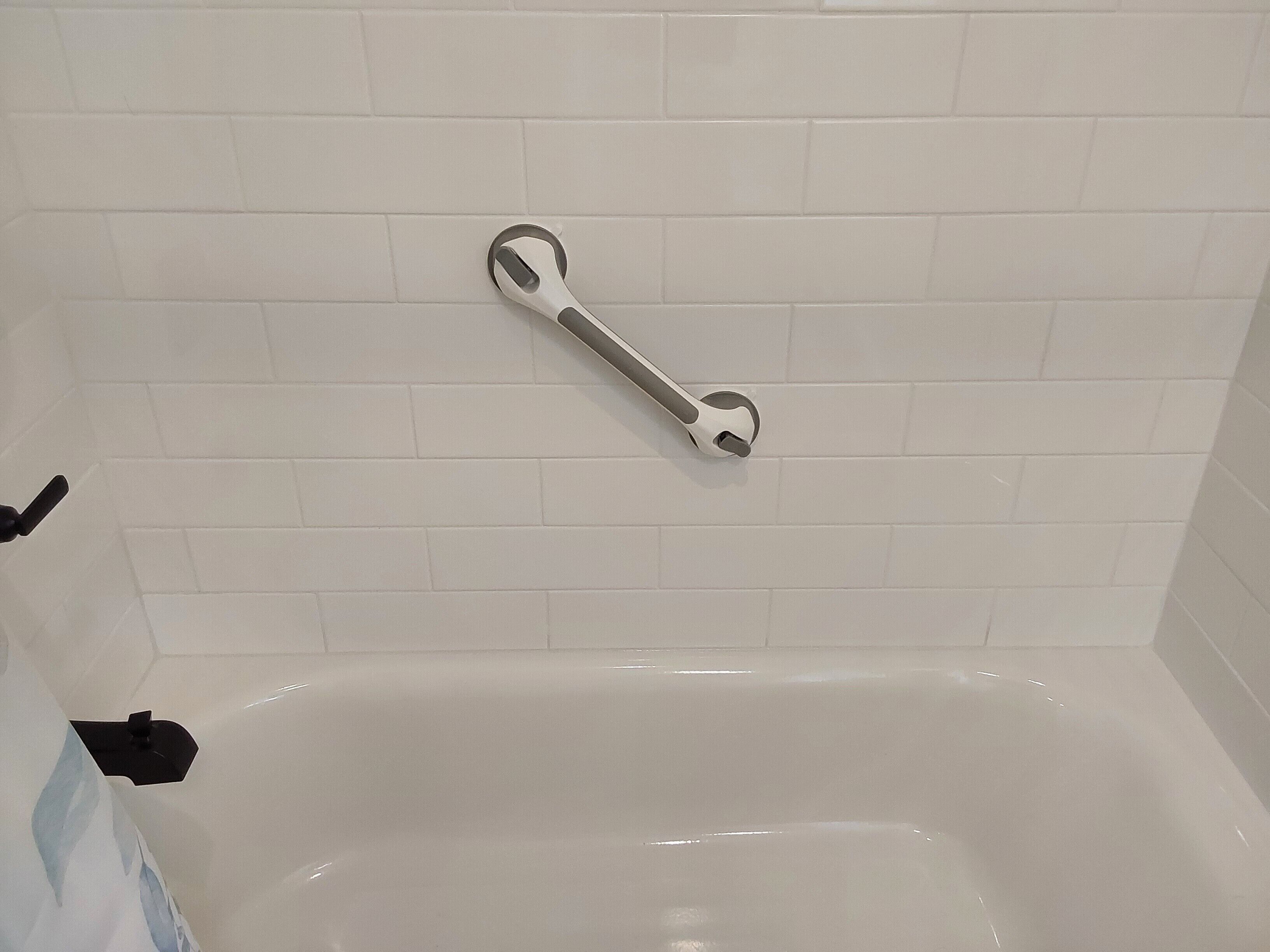 A bathroom with white tiled walls and a white bathtub.