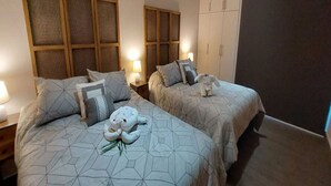 A bedroom with two beds, each with a geometric-patterned bedspread and matching pillows. There are bedside lamps, a wardrobe, and a decorative stuffed animal on one bed. - 2BD Beachfront Condo @ Playa Potrero (Provincia de Guanacaste)