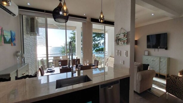 A modern kitchen with a large island, pendant lights, and a view of the ocean. - 2BD Beachfront Condo @ Playa Potrero (Provincia de Guanacaste)
