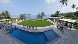 A swimming pool with a view of the ocean, surrounded by a white fence and palm trees. - 2BD Beachfront Condo @ Playa Potrero (Provincia de Guanacaste)