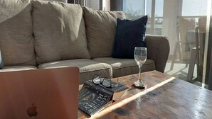 A modern living room with a sofa, a glass table, a laptop, and a wine glass. - 2BD Beachfront Condo @ Playa Potrero (Provincia de Guanacaste)