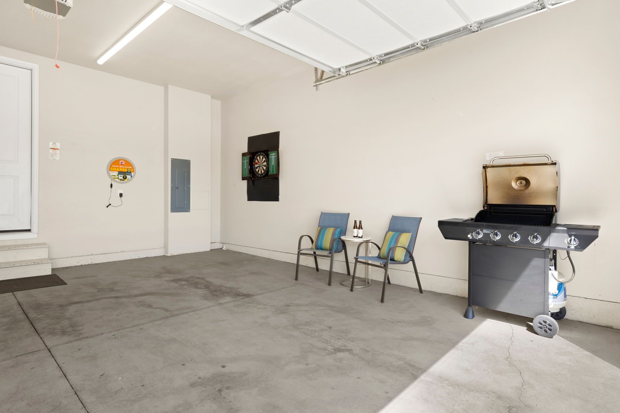 A spacious indoor area with a concrete floor, a grill station, two chairs, and a dartboard on the wall.