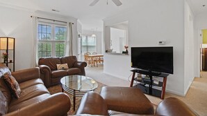 A living room with a ceiling fan, a television, and a dining area with a table and chairs.