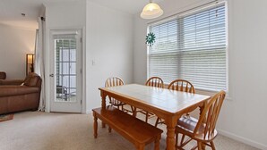 A dining area with a wooden table and chairs, a bench, a door with a glass panel, and a window with blinds.