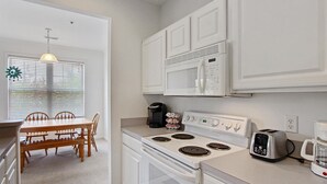A kitchen with white cabinets, a stove, a microwave, a toaster, and a coffee maker.