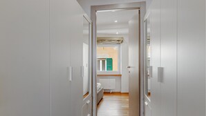 Ein schmaler Korridor mit Holzboden, der zu einem Raum mit Heizkörper und einem Fenster mit Jalousien führt.