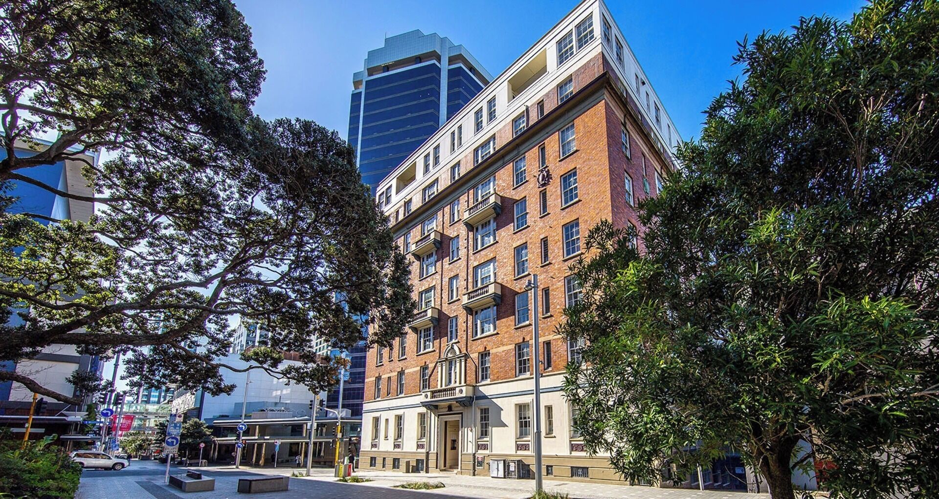 A multi-story building with a brick facade and large windows, surrounded by trees.