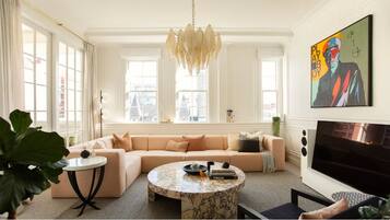 A modern living room with a beige sofa, a round marble coffee table, and a large window with curtains.