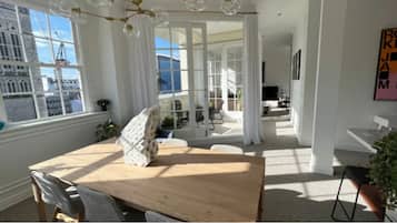 A bright room with a wooden table, white curtains, and a view of the outside.