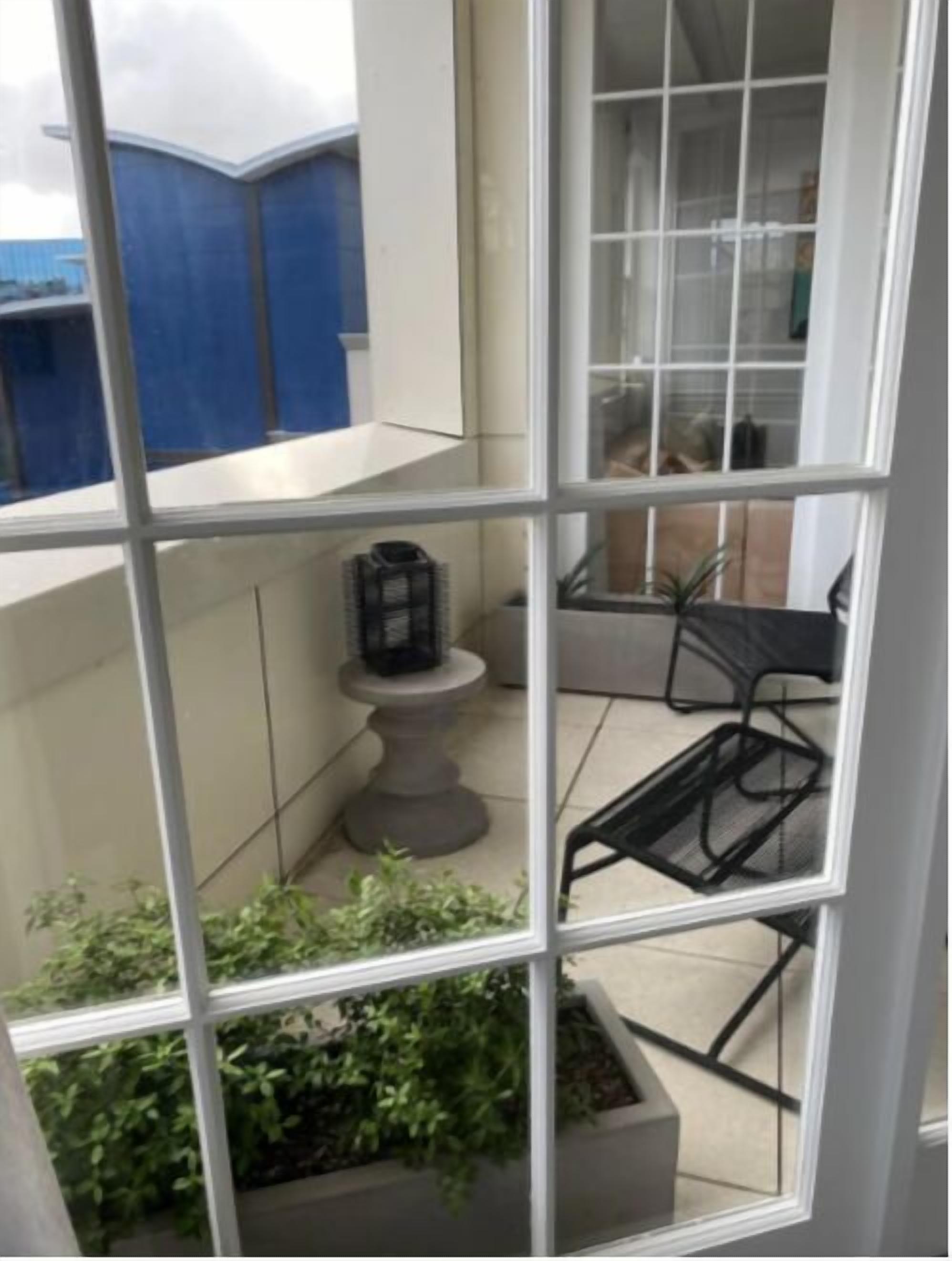 A view through a window of a room with a tiled floor, a small table with a chair, and a potted plant.
